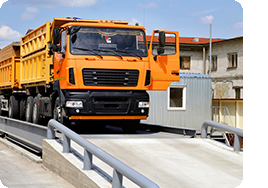 Orange truck with grain is weighed on the scales in the grain storage area.
